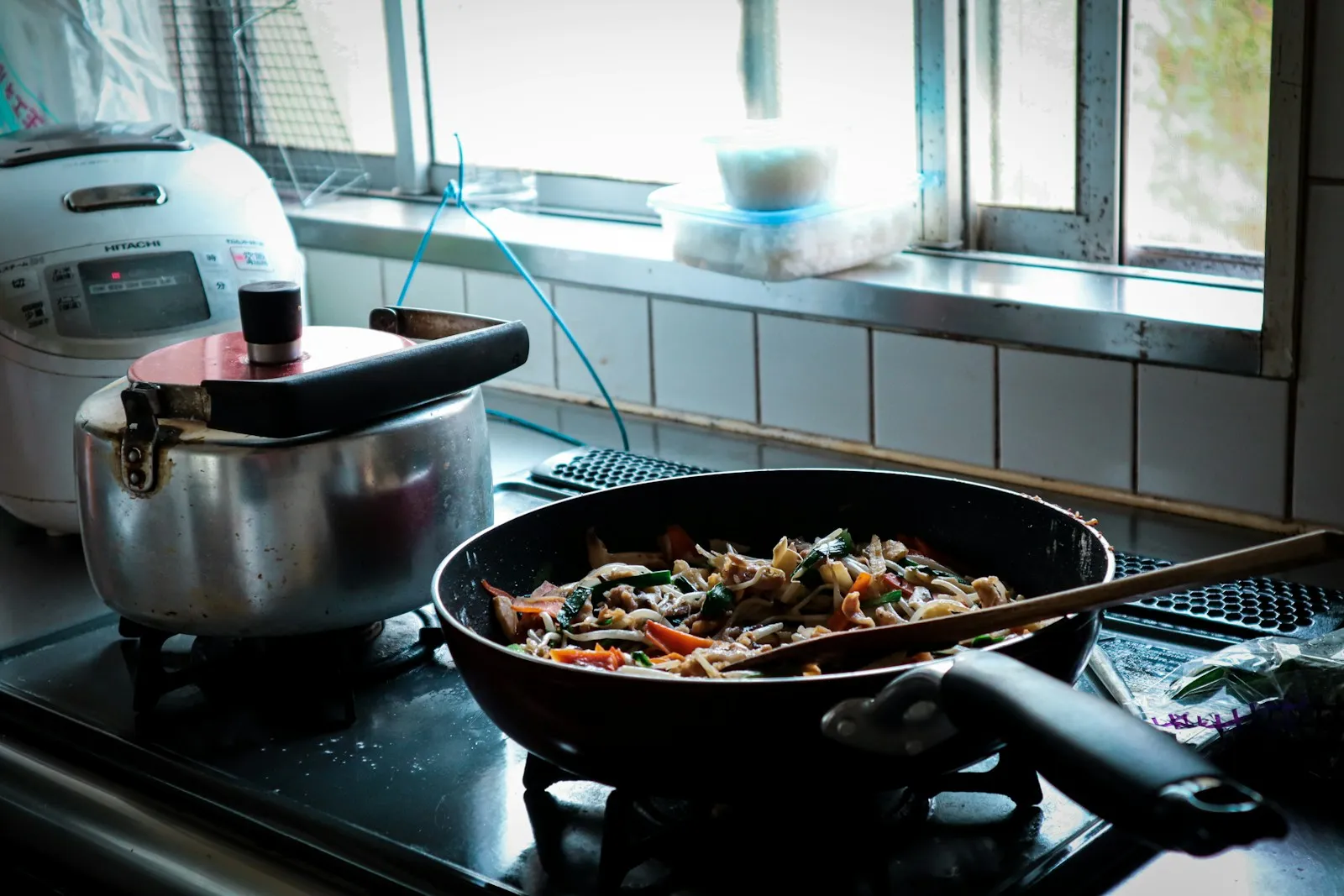 調理中のフライパンと炊飯器が並ぶ台所